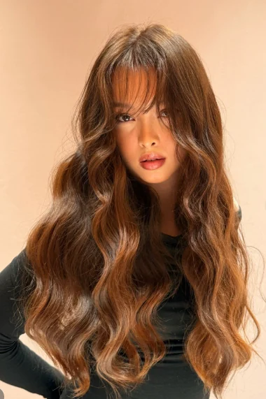 Long glossy waves with curtain bangs in a warm citrine balayage